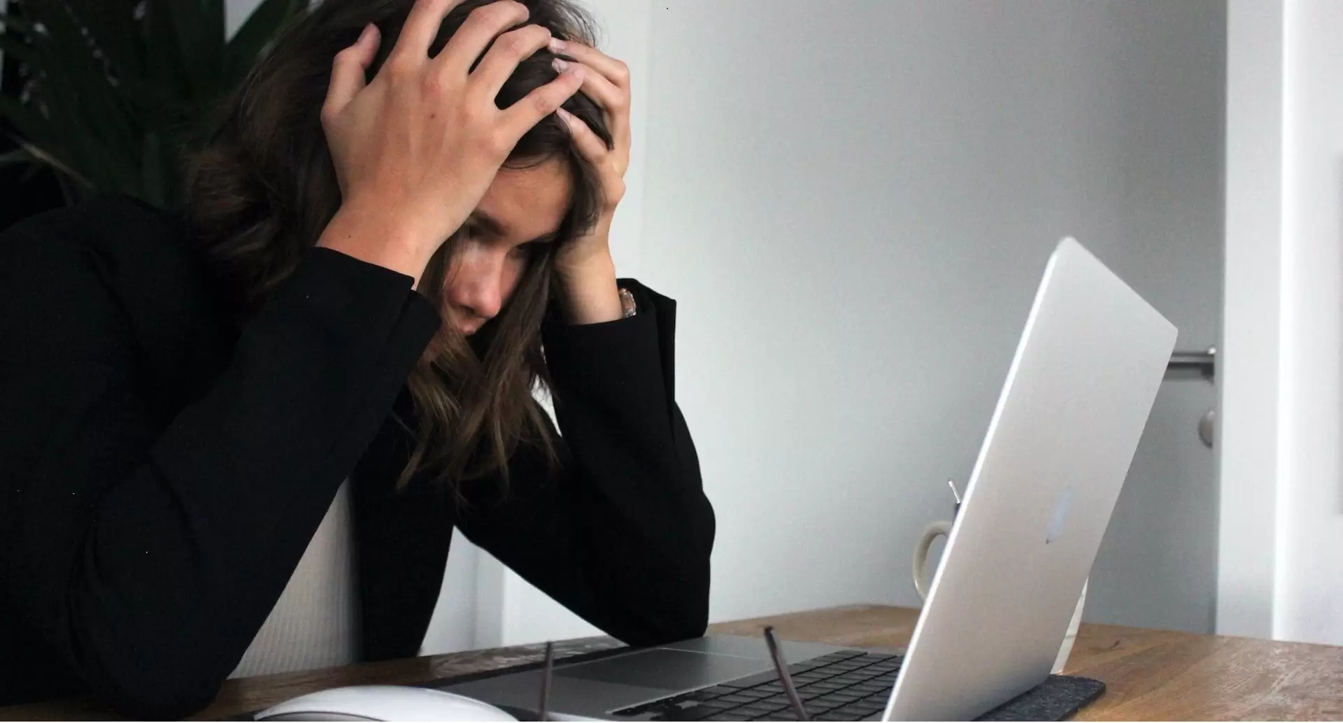 A woman holds her head in frustration while looking at her laptop screen.