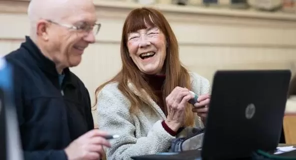 Elderly couple laugh as they look at laptop screen.